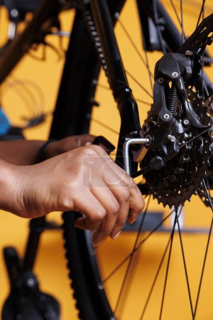 Close up of young black person adjusting bike rear derailleur with specialized equipment. Image focused on african american female hand holding an allen key to repair and maintain bicycle parts.