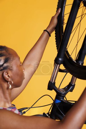 Photo for Close-up of african american female disassembling flat bicycle tire in order to fix and replace it. Detailed shot of young, fit, black woman carrying the wheel of the bike for additional maintenance. - Royalty Free Image