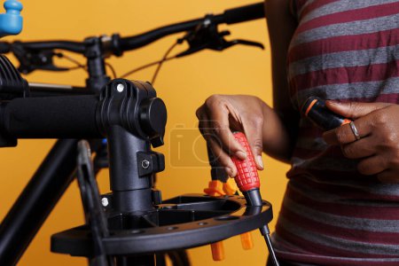 Close-up of african american female hand organizing necessary bicycle service tools. Photo focus on screwdriver and other specialized equipments being arranged on bike repair-stand by an individual.