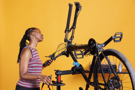 African american female meticulously examining bike components and fixing front fork with specialized tools. Young black woman inspects and maintains modern bicycle with care.