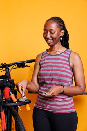 Femme afro-américaine engagée choisit soigneusement et inspecte divers équipements de kit de réparation de vélo professionnel. Femme noire énergique tient et organise des outils spécialisés pour l'entretien des vélos.