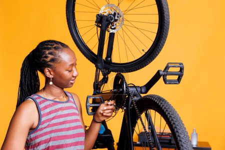 Sports-loving woman expertly adjusting broken bicycle crank arm with specialized multitool. Young african american lady carefully examining and fixing bike components with professional allen key.