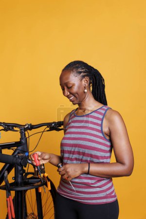 Close-up of black woman holding bicycle tools from a professional repair-stand for maintenance and adjustments. Detailed view of african american female assembling specialised equipment.
