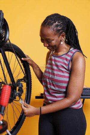 Amante de los deportes señora afroamericana asegurando y apretando el eje y el cubo de la bicicleta. Imagen que muestra a la joven activa mujer negra sosteniendo equipo profesional para el mantenimiento de bicicletas.