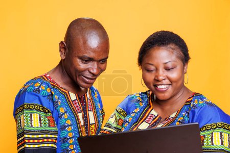 Téléchargez les photos : Homme et femme noirs joyeux avec le sourire sur le visage à l'aide d'un ordinateur portable et profiter de l'activité de loisirs Internet ensemble. Couple souriant à l'aide d'un ordinateur portable, vérifier les informations en ligne - en image libre de droit