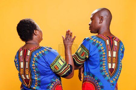 Woman rising hand up while chatting with man back view. African american couple wearing ethnic clothes speaking, girlfriend showing interrupting gesture while boyfriend talking