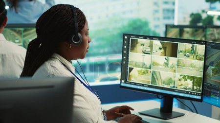 Un employé afro-américain surveille l'activité de la circulation dans la ville en utilisant le système de vidéosurveillance pour assurer la sécurité publique. Une femme regarde des vidéos de surveillance en temps réel dans la salle d'observation du gouvernement. Caméra A.