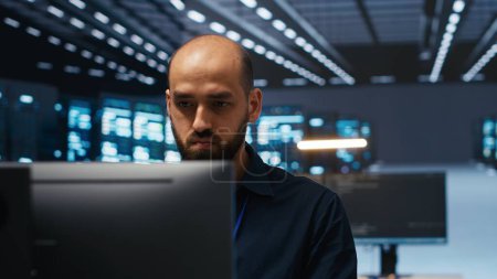 Hombre en la sala de servidores escribiendo código, asegurando que los datos permanezcan protegidos de amenazas. Captura panorámica del técnico de TI protegiendo supercomputadoras contra el acceso no autorizado, asegurando el sistema de los piratas informáticos