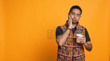 Foto de Hombre somnoliento bostezando y frotando los ojos. sorbiendo café para despertar y ganar energía. Persona agotada sintiéndose fatigada después de la noche sin dormir, bebiendo bebidas con cafeína, fondo del estudio, cámara B - Imagen libre de derechos