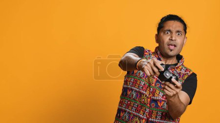 Photo for Gamer annoyed after losing online multiplayer videogame, being defeated by rival players. Indian man shocked and gutted after seeing game over message, holding controller, studio background, camera A - Royalty Free Image