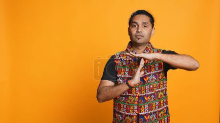 Portrait of assertive indian man asking for timeout, doing hand gestures, feeling fatigued. Firm person doing vehement pause sign gesturing, wishing for break, studio background, camera B