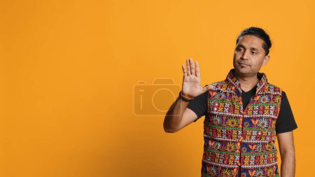 Hombre indio tratando de detener la lucha caótica usando el gesto calmante de la mano para difundir las tensiones, haciendo la resolución pacífica. Tranquilizar a la persona haciendo gestos de signos de calma, fondo del estudio, cámara A