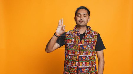 Indian man doing ok hand sign, feeling pleased, agreeing with satisfactory conclusion. Optimistic person doing okay symbol gesturing, offering positive feedback, studio background, camera B