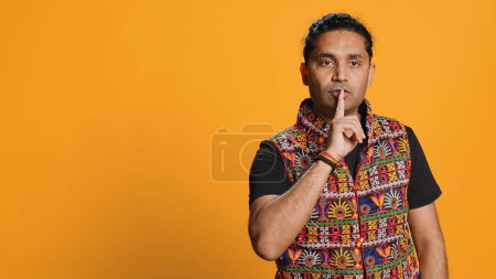 Authoritative man doing shushing hand gesturing, demanding secrecy, irritated by noise. Stern person complaining, placing finger on lips, doing quiet warning sign gesture, studio background, camera A