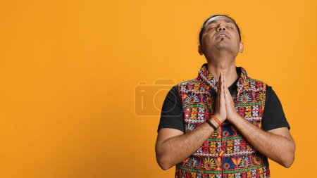Pious indian man praying to his god, asking for forgiveness. Spiritual person doing worship hand gesturing, confessing, begging for pardon, isolated over studio background, camera A
