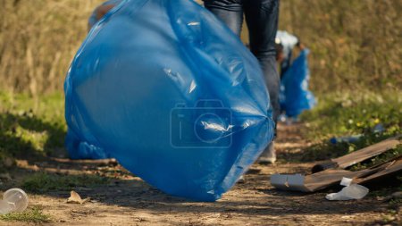 Diverse Aktivisten räumen Müll in einem Müllsack auf, Umweltschutzkonzept. Ehrenamtliche Helfer schützen das Ökosystem Wald und sammeln Müll mit Krallenwerkzeug ein. Kamera A.