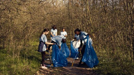 Foto de Grupo de voluntarios que trabajan para limpiar el bosque de la basura, recolectando basura y desechos plásticos en bolsas. Activistas ambientales acaparando basura y reciclaje, apoyan la justicia ecológica. Cámara B. - Imagen libre de derechos