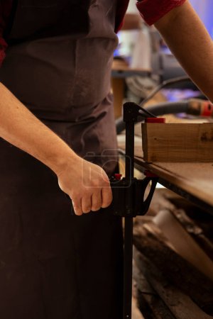 Kunsthandwerker mit Schraubstock zum Halten von Holzklötzen, Beginn der Holzkunst im Atelier, Nahaufnahme. Holzbearbeitungsspezialist in der Tischlerei mit Flügelklemme, um Stück Holz fest zu sichern