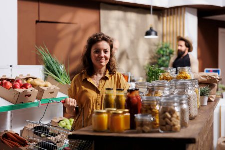 Portrait de femme souriante à la recherche de légumes frais dans un magasin écologique zéro déchet. Un client heureux faisant des courses, achetant des aliments biologiques biologiques dans un magasin de quartier local
