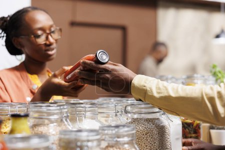 Un client afro-américain soucieux de l'environnement achète des produits frais et biologiques dans un éco-supermarché. Photo axée sur la femme parlant à un commerçant et choisissant des produits locaux sans plastique.