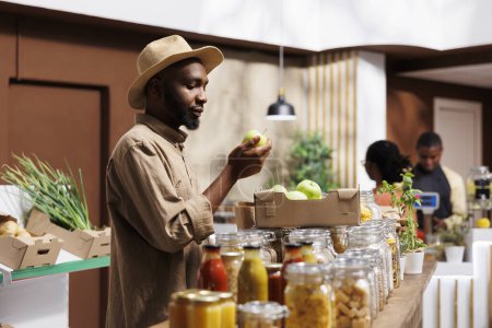 African American man explores fresh fruits and vegetables and admires sustainable, organic produce. The market supports local producers, offering nutritious options with a low carbon footprint.