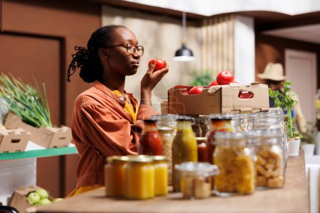 Magasins de femmes noires au marché local, soutenir les producteurs locaux et choisir des produits écologiques comme les fruits et légumes frais. Dame afro-américaine près du verre vérifiant les tomates.