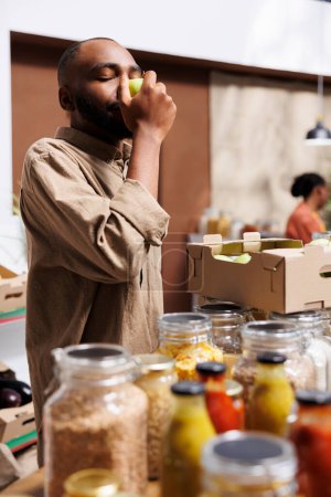 L'image montre un client afro-américain inhalant la fraîcheur d'une pomme verte dans un magasin local. Plan détaillé d'un homme noir tenant et admirant les fruits cultivés localement dans le magasin écologique.