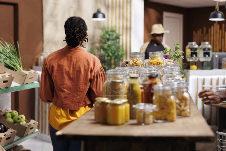 Black man selling variety of eco friendly, locally grown, and organic products. A customer browses and buys bulk items with reusable packaging, enjoying the freshness approach of the store.