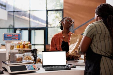 Blank white screen displayed on laptop while black woman with glasses receives her zero waste package. Isolated device with copy space for advertising or promotion of eco friendly bio food store.