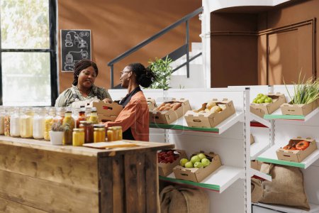 Le vendeur afro-américain vend des fruits et légumes frais et biologiques à l'épicerie verte. Un agriculteur local donne des caisses de produits biologiques fraîchement récoltés à une commerçante.