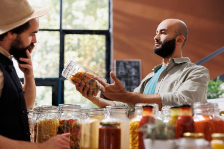 Ein junger Mann erkundet einen umweltfreundlichen Laden und betrachtet eine Vielzahl frischer Bioprodukte in Mehrwegverpackungen. Ein Kunde aus dem Nahen Osten untersucht Gläser mit Pasta und Getreide.