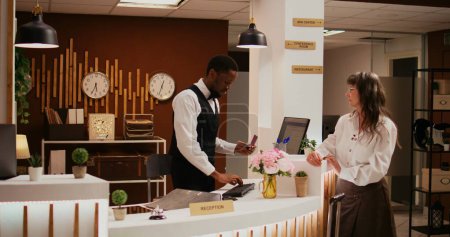 Afrikanisch-amerikanischer Arbeiter überprüft Pass-Ausweis an der Rezeption, bevor er sich für Zimmerreservierung, Concierge-Service anmeldet. Mitarbeiter unterstützen alte Frau beim Check-in, Gastgewerbe.
