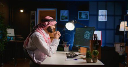 Licensed arabic engineer updating neural networks, writing intricate binary code scripts on computer. Middle Eastern man uses digital device programming to upgrade AI datasets at home