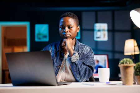 Programmeuse assise au bureau à domicile et écrivant du code sur minicomputer, créant un nouveau logiciel. Femme afro-américaine travaillant à distance, testant et recherchant des erreurs dans le programme sur ordinateur portable.