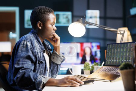 Afroamerikanerin analysiert Finanzdiagramme, betätigt sich im Online-Handel, studiert Wachstumstrends am Aktienmarkt, arbeitet von zu Hause aus. Schwarze Frau überprüft Status des Investitionswachstums auf Laptop.