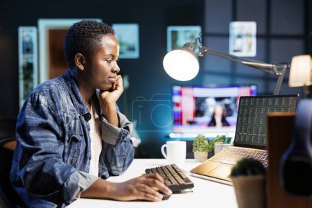 African American freelancer carefully analyzes financial data, comparing market trends and making strategic trading decisions online. Black woman concentrating on laptop showing trade trend values.