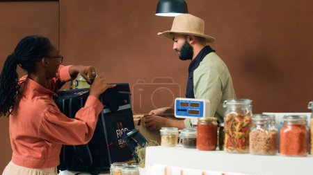 Photo for Merchant gives food order for delivery, putting homegrown organic vegetables in backpack. African american courier coming to pick up bio supermarket merchandise for local customers. - Royalty Free Image