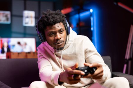 Gamer relaxing at home, sitting down on couch, excited to play games and enjoy leisure time. Man sitting on couch in apartment, playing videogame on gaming console, relaxing after work