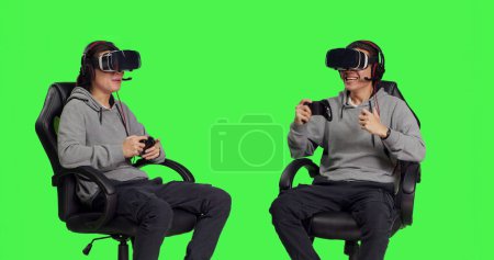 Téléchargez les photos : Joueur asiatique jouant à des jeux vidéo avec casque vr et joystick, s'amuser avec des appareils modernes. Jeune adulte appréciant le défi de jeu en ligne rpg, assis sur fond d'écran vert. - en image libre de droit