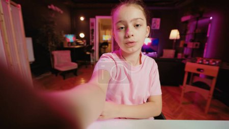 Kinderfilme im POV-Stil mit Smartphone im rosafarbenen neonbeleuchteten Wohnzimmer, das als professionelles Studio genutzt wird. Junger Online-Star filmt mit Selfie-Handykamera und diskutiert über lustigen Schultag