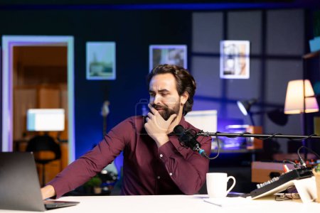 Téléchargez les photos : Man reading from laptop in studio, looking perplexed at recent news headlines, sharing opinions with audience. Show host talking with subscribers, feeling shocked by information he found online - en image libre de droit
