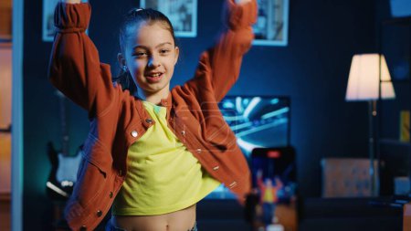Children media star dancing in apartment, recording video with phone for gen z internet users. Happy girl filming herself with smartphone doing dance moves, following online choreographic trends