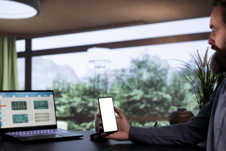 Business owner analyzing blank mockup display on smartphone, working with modern device at his mountaintop opulent cabin. Entrepreneur looking at white copyspace screen, wealthy lifestyle.