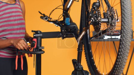 Mécanicien afro-américain utilisant différents outils pour réparer les poignées de guidon de vélo endommagées, fond de studio. Employé utilisant des engins spécialisés pour fixer les levier de vitesse et de frein sur la bicyclette, caméra A