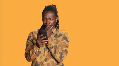 Photo for Modern guy navigating online websites on smartphone, checking his chats for texts and posing on camera. African american person using mobile apps to stay connected with friends. Handheld shot. - Royalty Free Image
