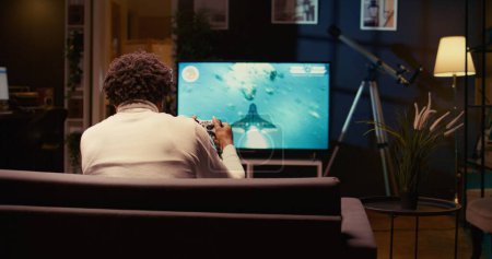 Mann im Heimkino nutzt Cloud-Gaming-Dienst, um anspruchsvolles Science-Fiction-Videospiel im Fernsehen zu spielen. Gamer genießen hochwertige Grafik, Streaming-Spiel über das Internet, Schwenk-Shot