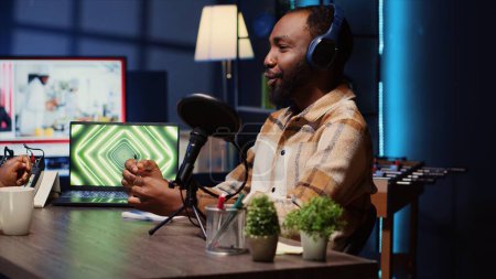 Gast in einer Internet-Podcast-Show, die dem Moderator interessante Geschichten erzählt und die Fans während der Live-Übertragung in ihren Bann zieht. Afrikanischer Mann im Studio teilt Fakten neben 3D-Animationen auf Laptop