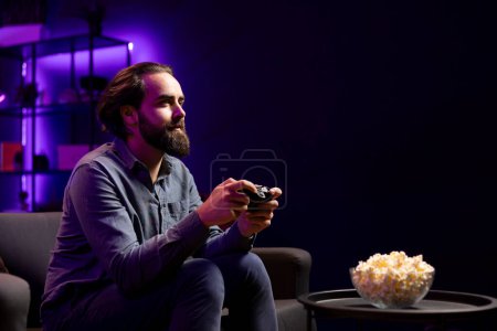 Gamer, die sich mit modernster Spielkonsole und Gamepad an einem Online-Multiplayer-Turnier beteiligen, während sie Popcorn essen. Mann im Heimkino spielt Videospiele und konsumiert Snacks