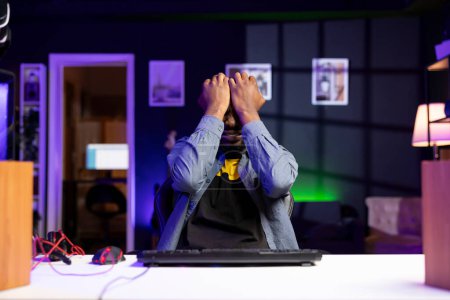 Hombre lloroso molesto después de perder mientras juega videojuegos en PC de juego en el apartamento tarde en la noche. Retrato del jugador irritado frustrado con la derrota durante el juego multijugador, llorando de ira