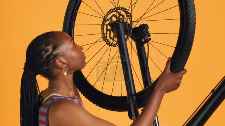 Femme détachant roue de vélo et le guidon de réglage dans l'atelier de réparation arrière-plan studio. Cyclisme amateur démontage pneu de vélo, réparation de composants avec un équipement professionnel, caméra A